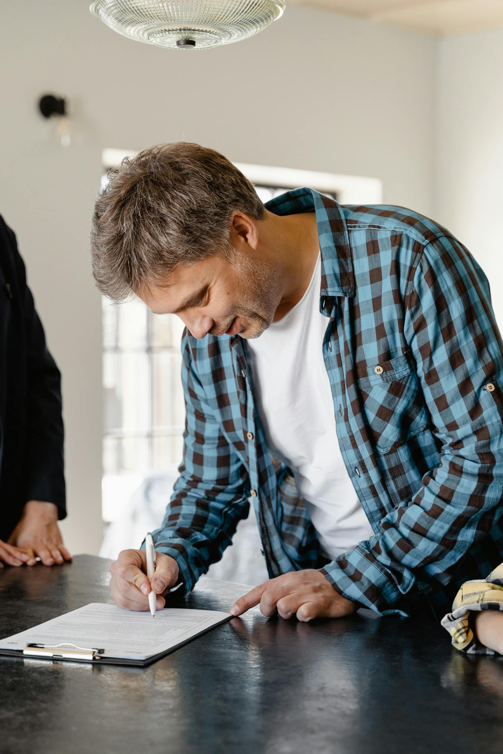 A man signs important papers in a stylish home setting, symbolizing a new start.