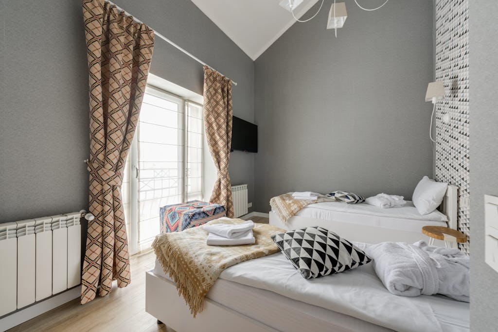 Stylish bedroom with twin beds, patterned curtains, and wall-mounted TV.